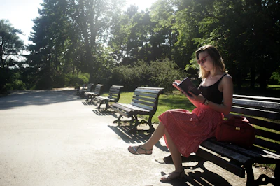 Sunlit park bench with a novel resting beside a pair of reading glasses