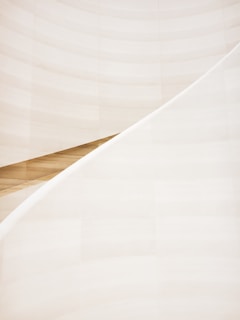 A minimalist and abstract architectural element featuring smooth, sweeping curves and soft lines. The scene is dominated by light, creamy hues with a slight gradient effect. The composition highlights the elegant and simple beauty of architectural design.