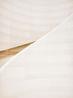 A minimalist and abstract architectural element featuring smooth, sweeping curves and soft lines. The scene is dominated by light, creamy hues with a slight gradient effect. The composition highlights the elegant and simple beauty of architectural design.