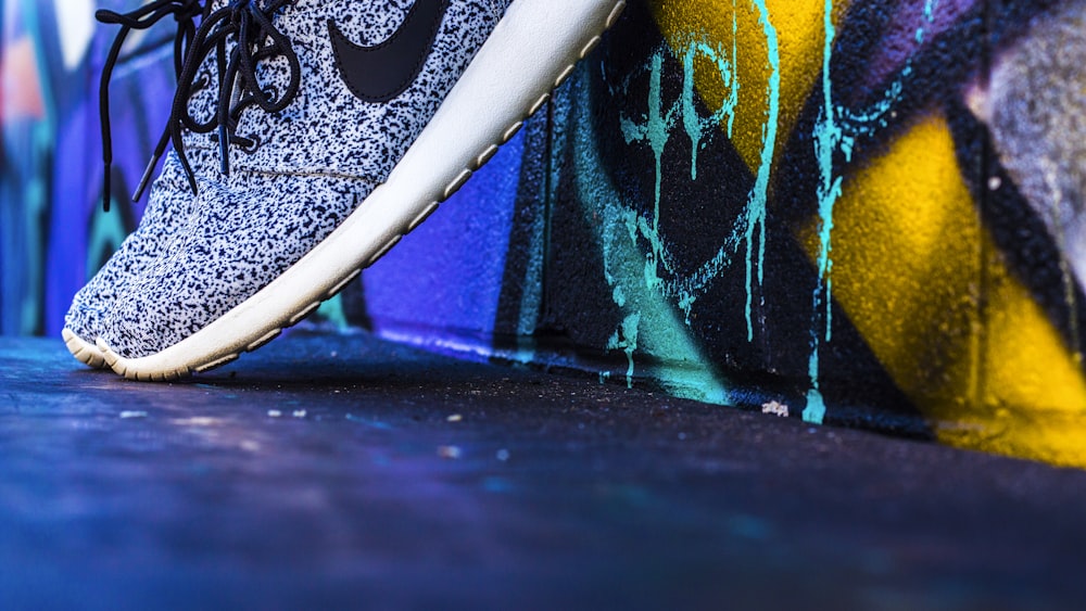 unpaired gray and white Nike sneaker leaning on concrete wall with graffiti