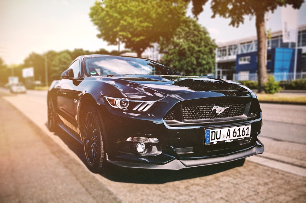 shallow focus photography black Mustang sports car parked beside the street