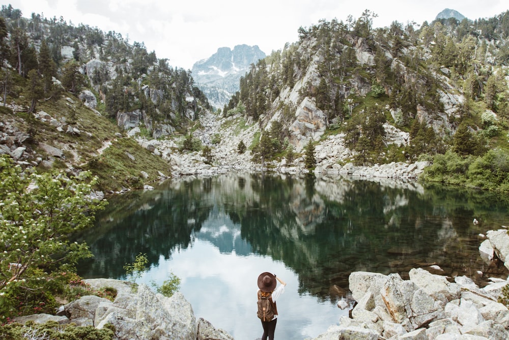 person standing in front of body of water between rock mountain