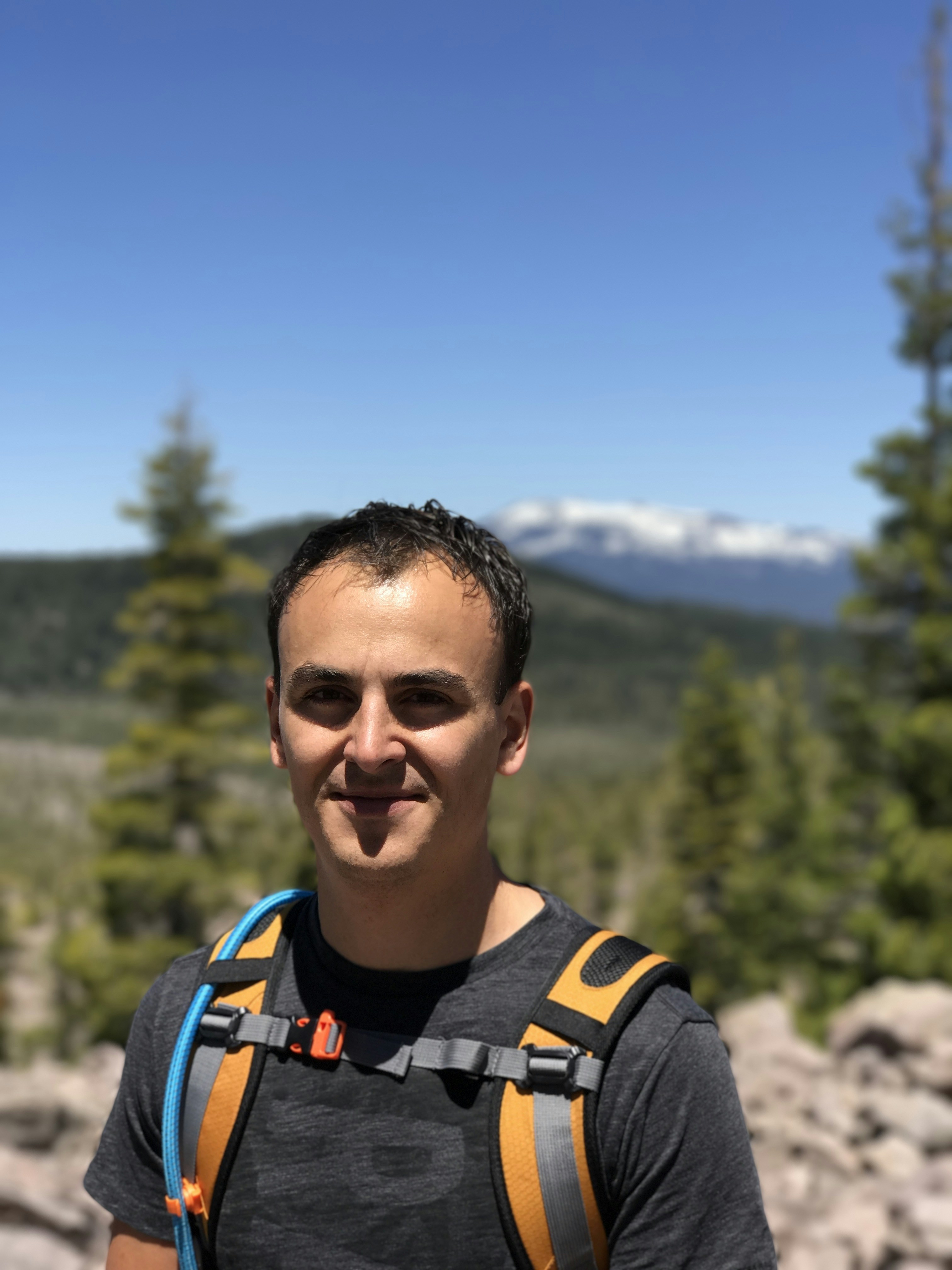 Young Indian man with backpack smiling in front of Himalayan mountain landscape