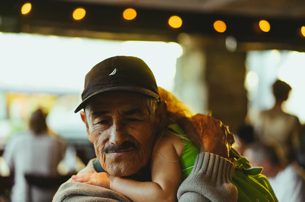 An older man smiling as he is held from behind by his family