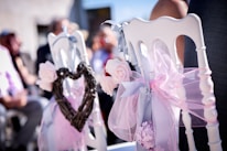 Close-up of delicate white flowers decorating wooden chairs in an outdoor wedding setting.