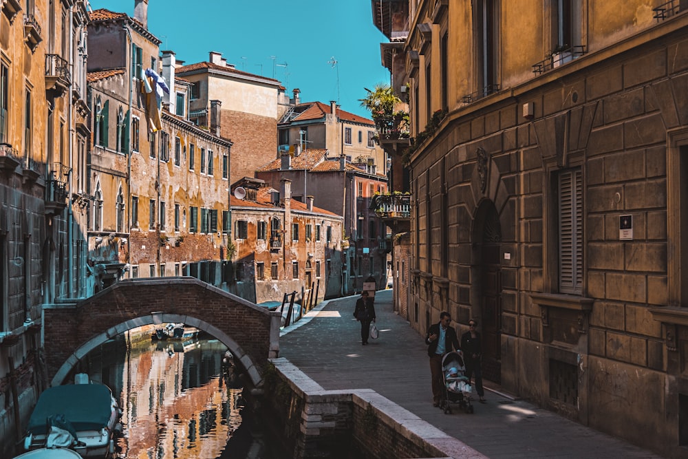 three people walking on alleyway beside canal during daytime