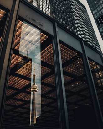 glass panel wall of building displaying the reflection of CNN Tower
