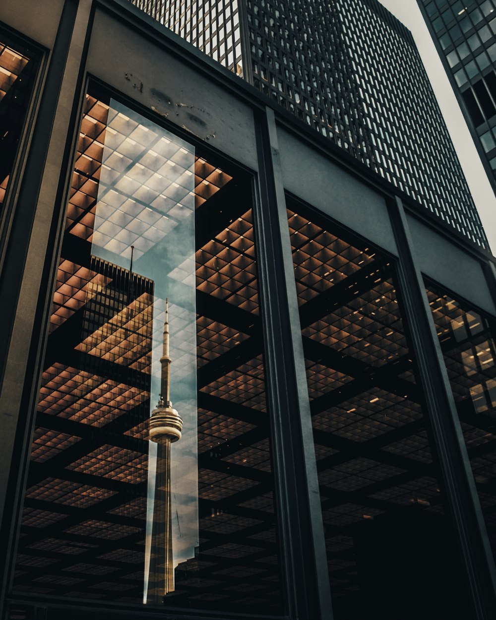 glass panel wall of building displaying the reflection of CNN Tower