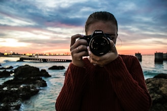 photo of woman holding black Canon DSLR camera near body of water