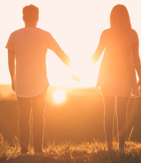 man and woman holding hands white facing sunset