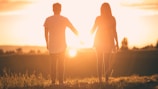 Un homme et une femme se tenant la main debout dans un champ face à un couché de soleil.