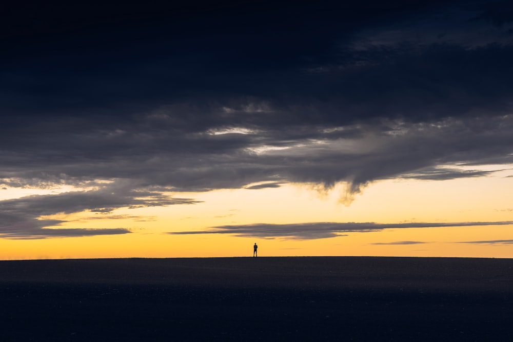 silhouette of person standing on hill during sunset