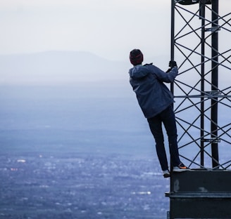 man climbing on tower near buildings at daytime