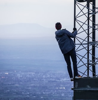 man climbing on tower near buildings at daytime