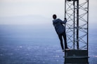 man climbing on tower near buildings at daytime