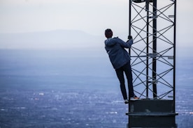 man climbing on tower near buildings at daytime