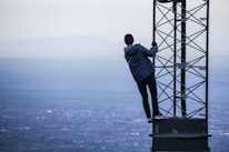 man climbing on tower near buildings at daytime