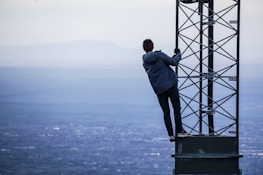 man climbing on tower near buildings at daytime