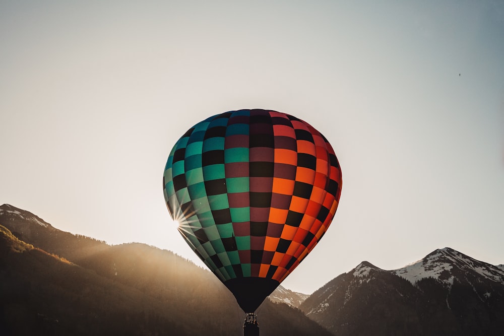 昼間、山の近くを飛ぶ赤、黒、緑の熱気球