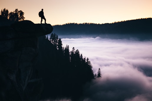 A person standing on a cliff, looking out over a vast landscape at sunrise, symbolizing new perspectives and bold actions.