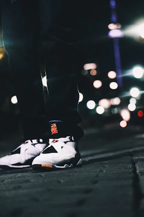 Model showcasing a sleek pair of RAMONEY sneakers on a city sidewalk at dusk.