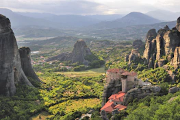 A peaceful monastery nestled among lush green hills under a clear blue sky.
