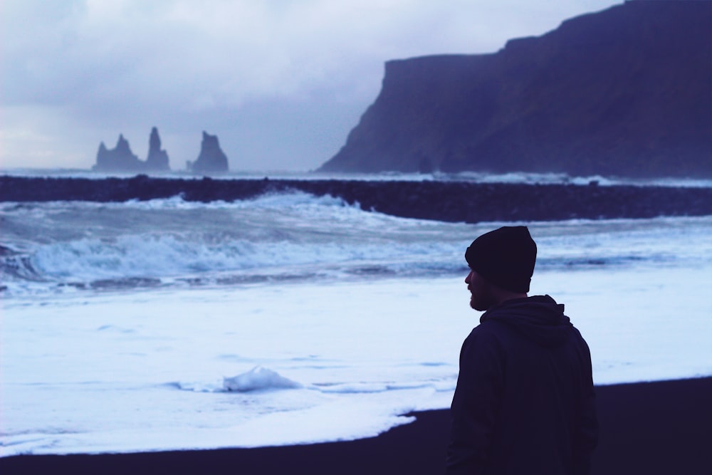 Mann steht am Meeresufer und schaut auf Wasserwellen