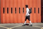man wearing black hat and white dress shirt walking on street near orange gate