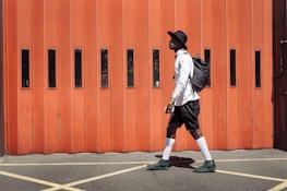 man wearing black hat and white dress shirt walking on street near orange gate