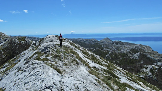 A hiker consulting a detailed map on a mountain ridge under clear skies.
