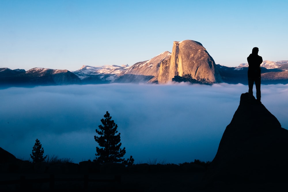 person standing on cliff watching sea of clouds