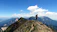 A smiling hiker standing on a rocky ridge overlooking a vast mountain valley at sunrise.