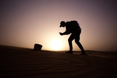 Traveler holding a phone with a weekly Qatar eSIM plan activated, standing near a desert dune at sunset