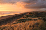 Crimson and orange hues painting the horizon over a rugged Australian coastline at dusk.