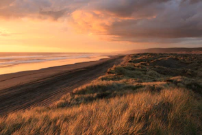 Crimson and orange hues painting the horizon over a rugged Australian coastline at dusk.