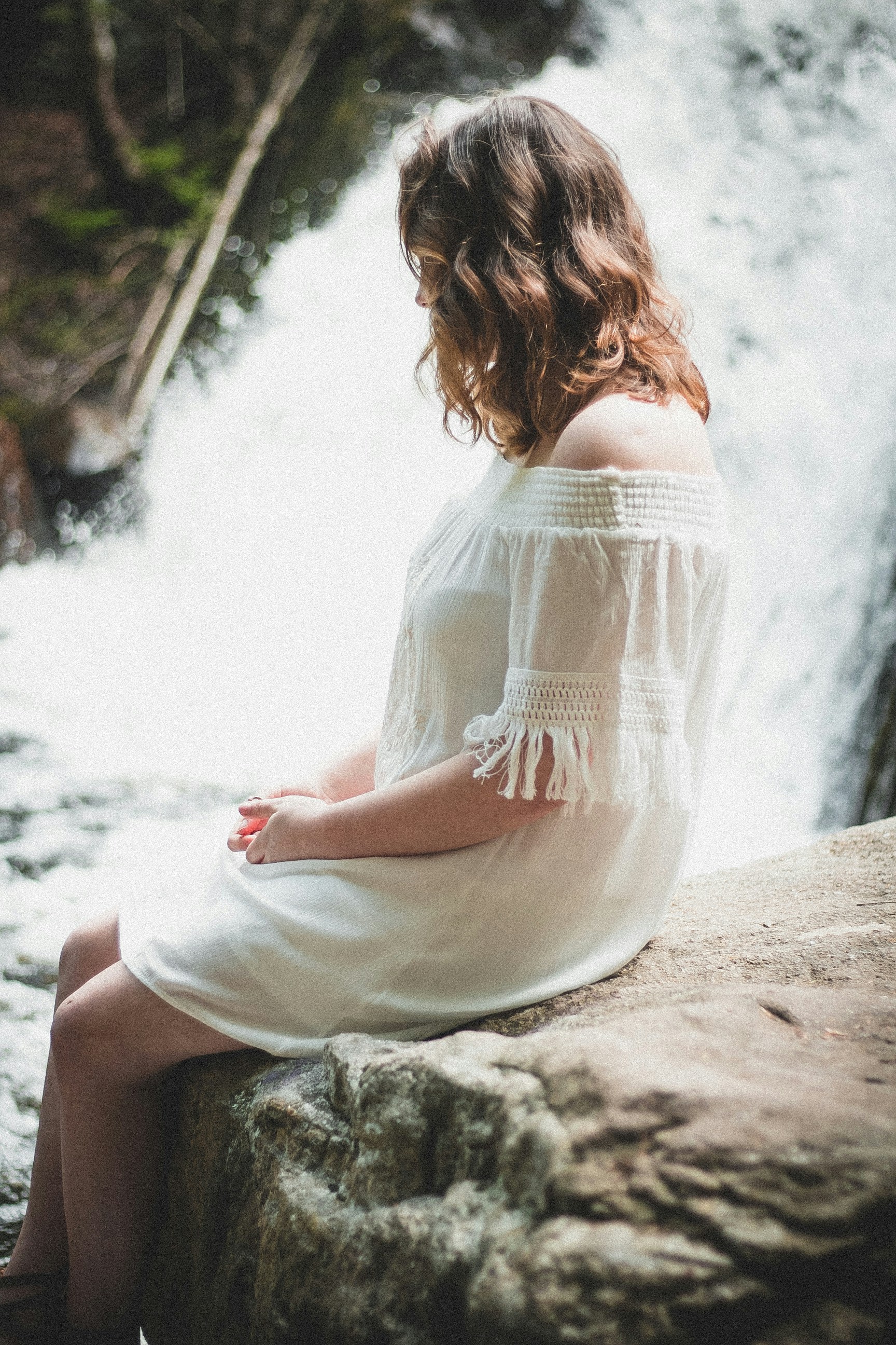 woman sitting on rock beside waterfall at daytime