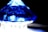 A faceted blue crystal or gemstone with a pyramid-like shape is positioned dramatically against a dark background. The light plays off the facets, creating a vibrant mix of blue and white reflections.
