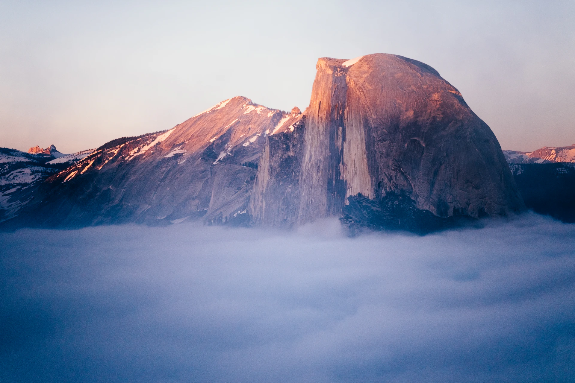 A breathtaking view of Yosemite's Half Dome at sunrise, with golden light illuminating the rugged granite peak and surrounding forest.