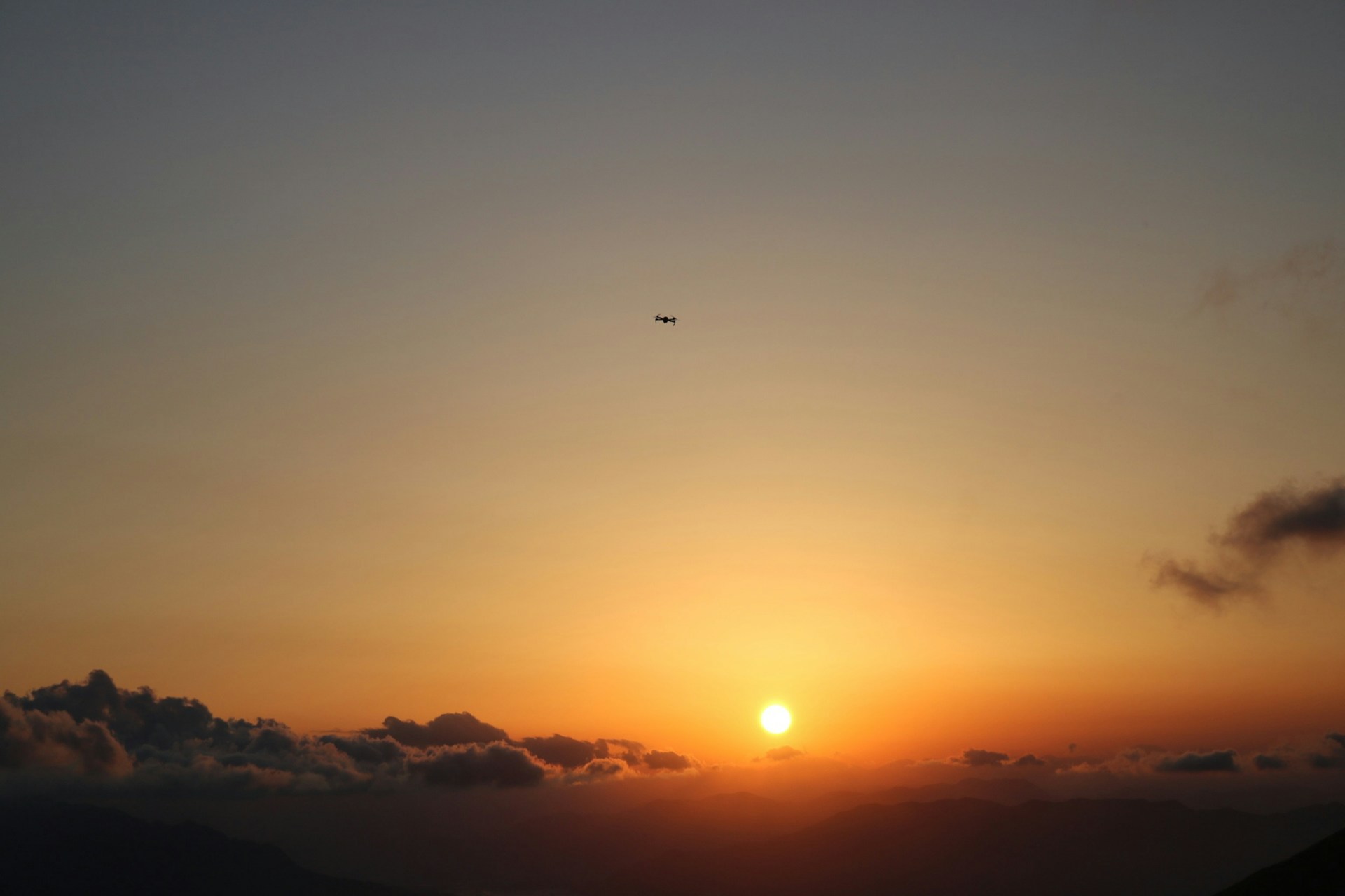 A warm, golden-hued drone shot capturing the vast, rugged outback landscape at sunset, with soft beige and chocolate brown tones blending into the horizon.