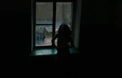 A silhouette of a woman by a window at sunset, evoking intimacy and secrecy.