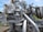 A complex and intricate assembly of industrial machinery featuring various interconnected pipes, valves, and mechanical components, with visible signs of rust and wear. The machinery is set against a backdrop of green grass and a clear blue sky.