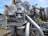 A complex and intricate assembly of industrial machinery featuring various interconnected pipes, valves, and mechanical components, with visible signs of rust and wear. The machinery is set against a backdrop of green grass and a clear blue sky.