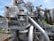 A complex and intricate assembly of industrial machinery featuring various interconnected pipes, valves, and mechanical components, with visible signs of rust and wear. The machinery is set against a backdrop of green grass and a clear blue sky.