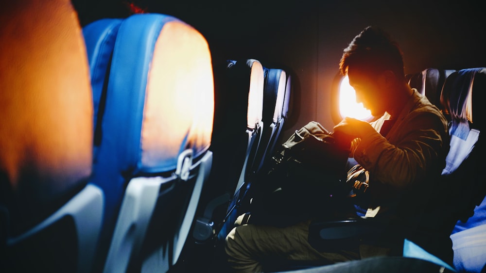 A man in an airplane seat looking into his backpack as setting sun shines through the window