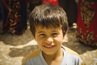 A candid shot of Bivin Lal holding a camera, smiling warmly in a sunlit outdoor setting.