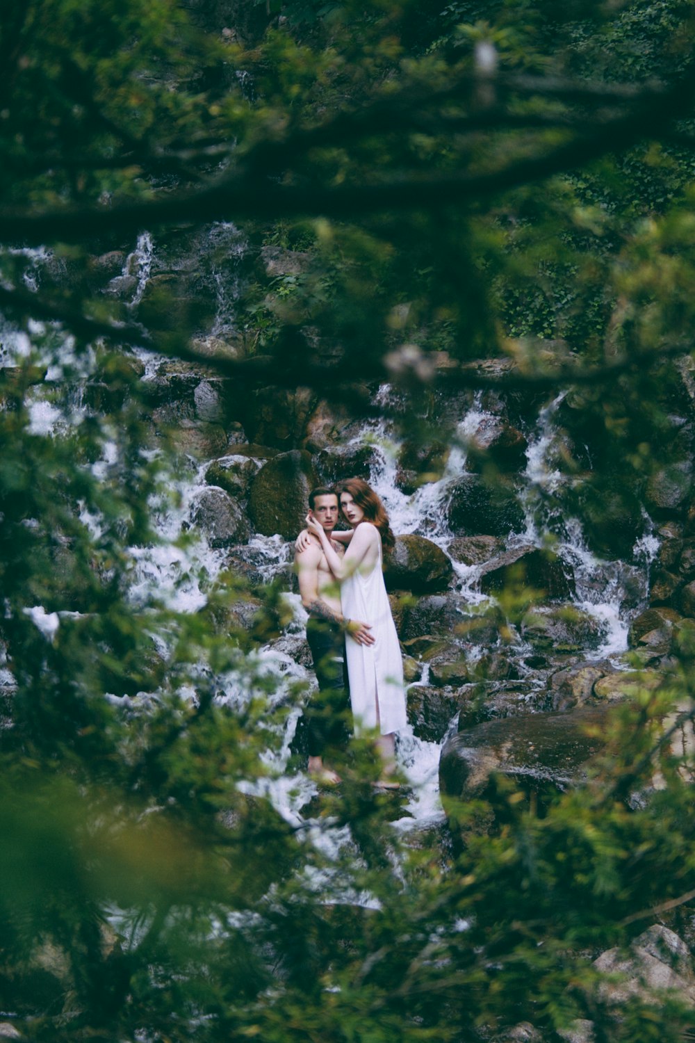 Homem e mulher abraçados em água corrente cercados por pedras
