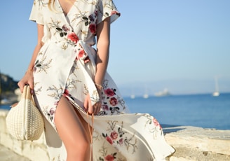 woman walking on seaside while holding woven bag