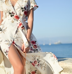 woman walking on seaside while holding woven bag