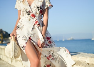 woman walking on seaside while holding woven bag