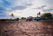 Wide shot of a tractor pulling implements across a vibrant green field at sunrise.